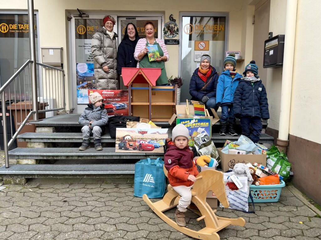 Spendenübergabe Kinder mit vielen Spielsachen vor Tür der Tafeln